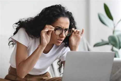 женщина в очках пытается что-то увидеть на экране ноутбука