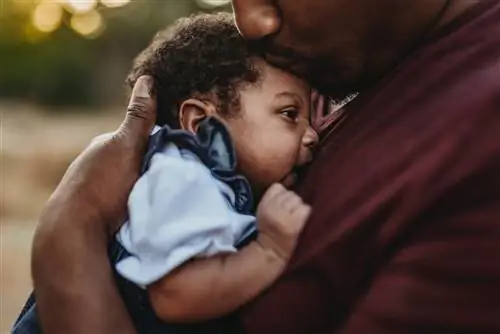 Папа прижимает к груди своего новорожденного ребенка.