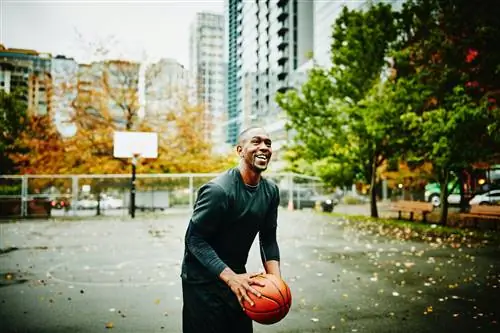 Пожилой мужчина играет в баскетбол на открытой площадке.