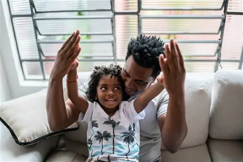 Пока они разговаривают, мальчик сидит на коленях у отца на диване.