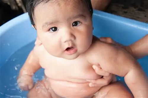 Голый пухлый ребенок принимает ванну.