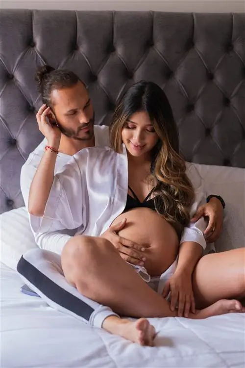 Муж целует живот беременной жены дома. Они счастливо проводят время вместе.