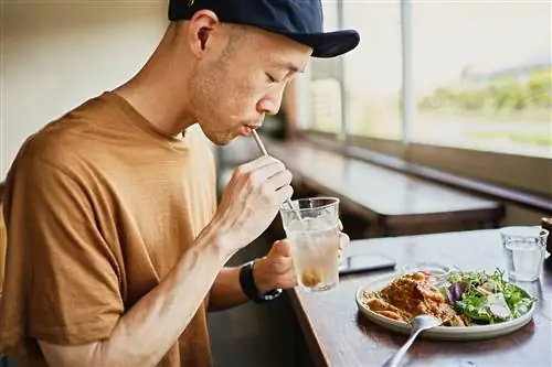 Мужчина пьет из стакана и ест здоровый обед.