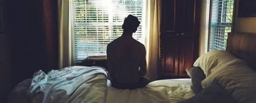 Мальчик сидит один на своей кровати и смотрит в окно