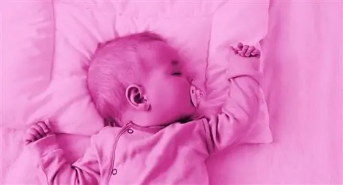 Розовая фотообработка ребенка, спящего на спине, положив голову на подушку.