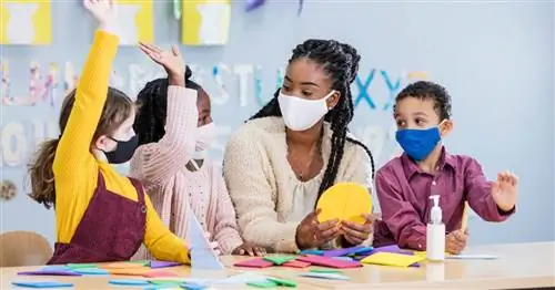 Черная учительница сидит с тремя учениками, обучая их