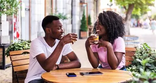 Пара сидит снаружи за столом, пьет и разговаривает