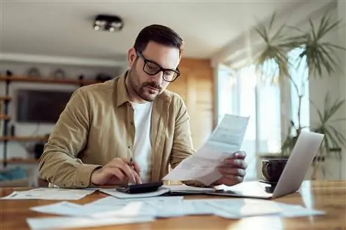 Молодой человек использует калькулятор во время работы над своими финансовыми планами дома.