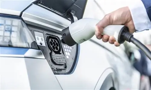 Водитель электромобиля вставляет электрический разъем для зарядки аккумуляторов.