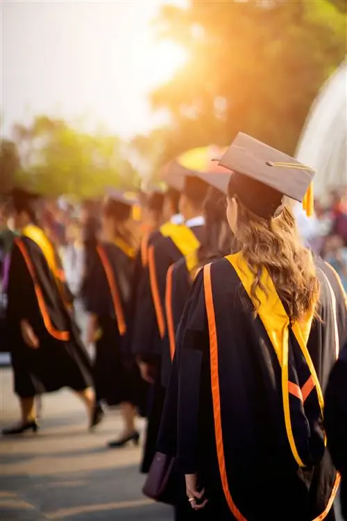 Вид сзади на выпускников университета, выстроившихся в очередь на вручение дипломов на церемонии вручения дипломов университета. Чт…