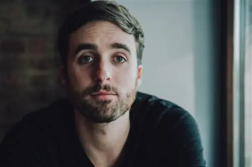 Мужчина с темными кругами под глазами смотрит вперед.