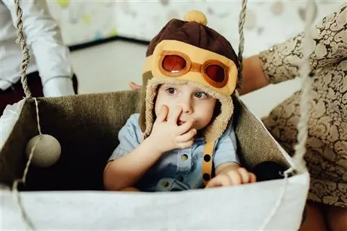 Счастливый ребенок играет и ковыряется в носу в корзине на воздушном шаре ручной работы.