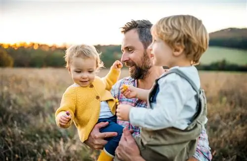 Отец держит двух малышей в поле