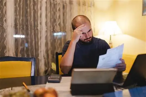 Лысый молодой человек выглядит обеспокоенным, просматривая свои счета дома.