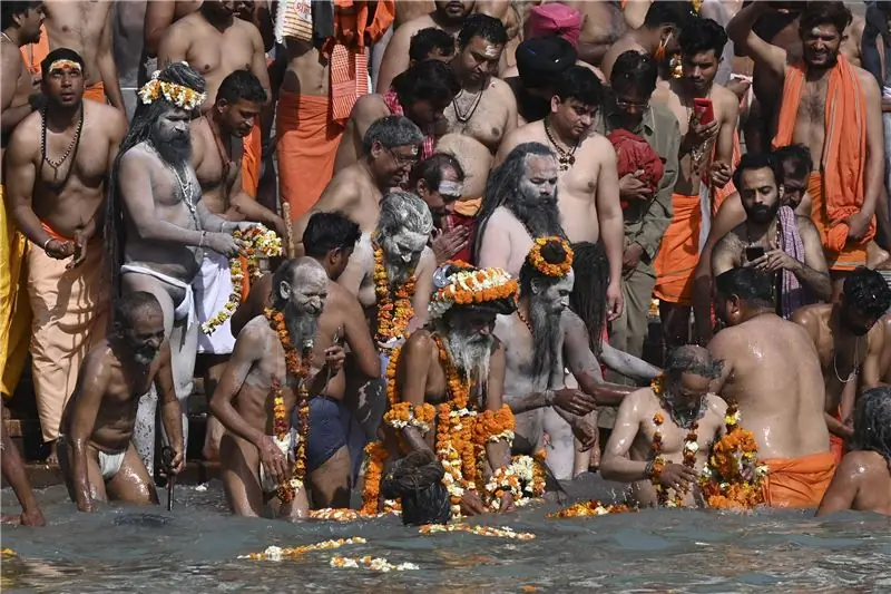 Мужчины стоят плечом к плечу у кромки воды. Большинство из них обнажены выше пояса. Многие носят цветы и оранжевую одежду